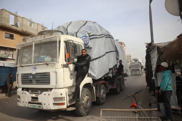 Men stand guard on the side of a truck carrying humanitarian aid as it drives on the main Salah al-Din Street in the Nuseirat refugee camp, central Gaza Strip on December 7 [File: Eyad Baba/AFP]