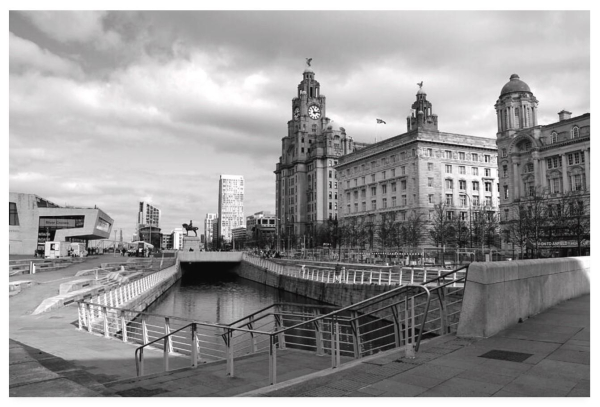 Black and white cityscape photograph showing very grand city buildings to the left of the shot, a statue in the distance to the right, and grey clouds above.