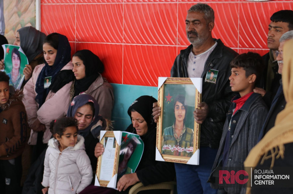 The family of Arab YPJ fighter Aruba Ali al-Kuno looks on, her father and mother carrying a picture of the martyr.