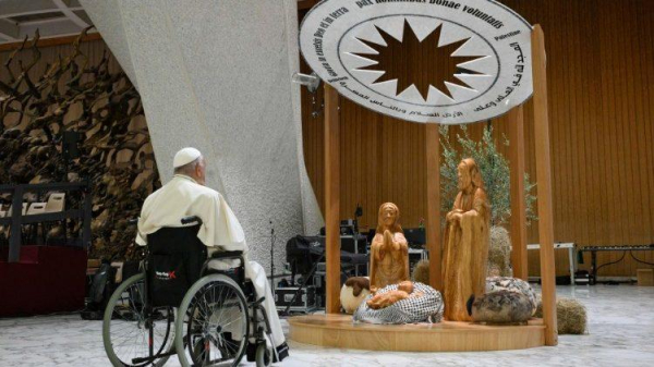 Pope Francis before the "Nativity of Bethlehem 2024" in the Paul VI Hall. The puppet that is supposed to be baby Jezus is lying on a keffiyeh. Above it a roof with words written among others in English and Arabic. (Source of image : https://www.vaticannews.va/en/pope/news/2024-12/pope-enough-with-wars-and-violence-in-the-world.html)
