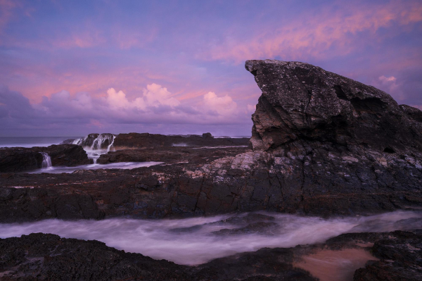 pink-magenta seascape sunset among the rocks and near a large fin-shaped boulder