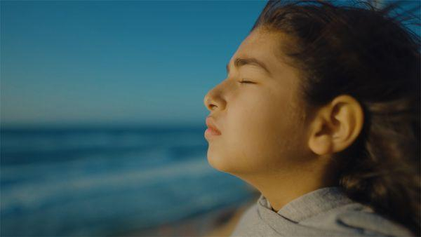 A still from the film Charm, part of From Ground Zero. A Palestinian girl stands on a beach, eyes closed, facing the sea.