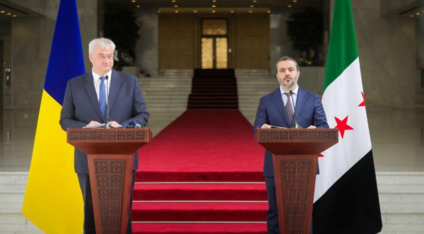 Ukraine's Foreign Minister Andrii Sybiha

Foreign Minister for the interim Syrian government Asaad Hassan al-Shibani

standing at podiums in front of their country's flags