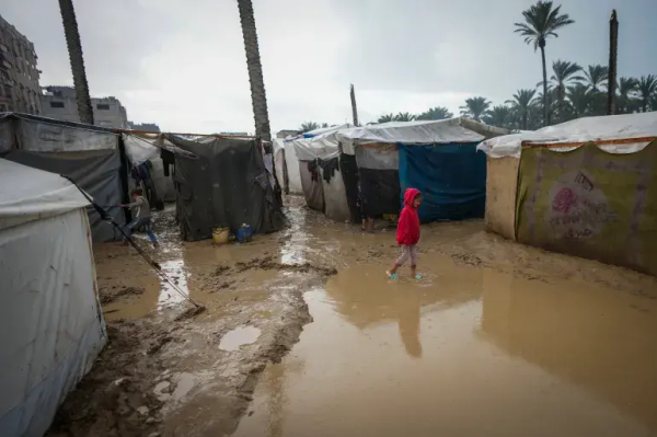 A young girl walks through a flooded street following overnight rainfall [Abdel Kareem Hana/AP Photo]