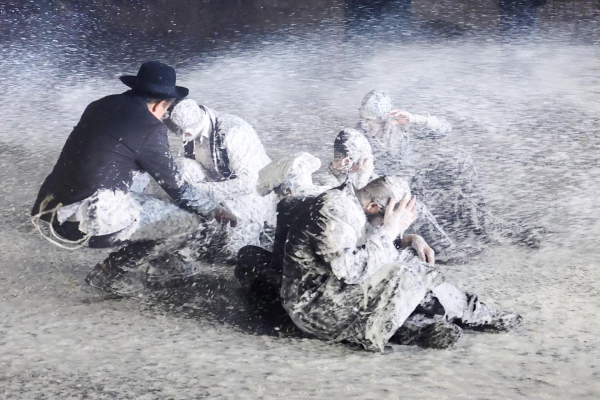 The men, holding up their hands to protect their faces, look almost like statues - except for one who has managed to remain above the fray and assist the man beside him. The spray is so intense it has obscured their faces and the background, contributing to the impression of a moment frozen in time and space.