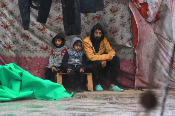 Palestinians take shelter from the rain at a makeshift camp in southern Khan Younis [Bashar Taleb/AFP]

2 children and a man are sitting on a stool in a flooded tent.