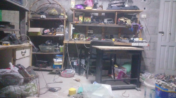 Photo of Ramy's DIY electronics lab. There is a desk and chair and many shelves filled with electronics equipment. The lab has since been destroyed.