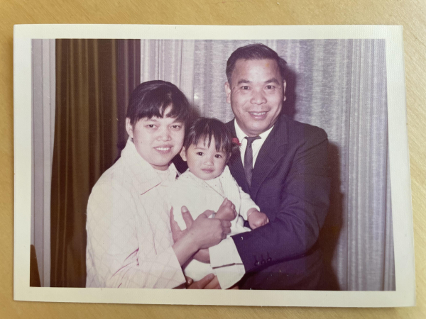 A little girl being held by both her mother and father. They all look happy. There is an obvious square in the middle where the colour is faded. 