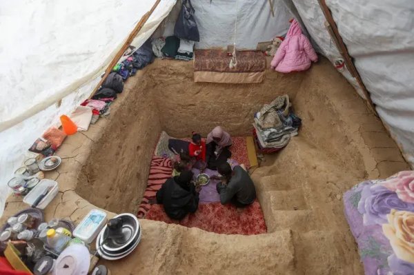 Palestinian Tayseer Obaid eats with his family in an underground pit he dug to protect from Israeli attacks at the tent encampment in Deir el-Balah, central Gaza [Ramadan Abed/Reuters]