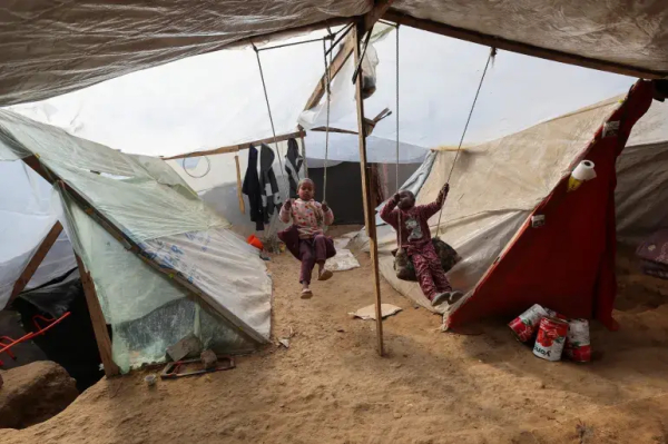 Children play on a makeshift swing set at the encampment in central Gaza [Ramadan Abed/Reuters]