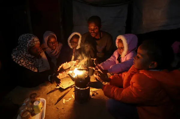 Obaid and his family warm themselves by a fire in their underground Deir el-Balah shelter [Ramadan Abed/Reuters]