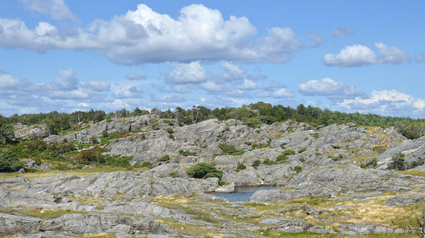 A photo of a hilly rocky landscape. The sky is blue with white clouds in it.