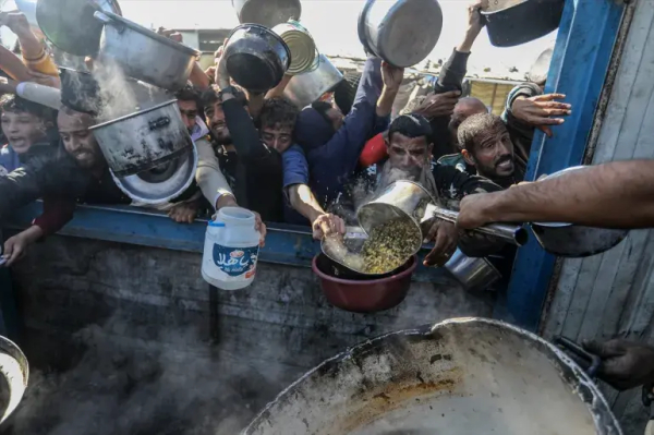 Palestinians reach out to receive food with their empty containers as charitable organisations distribute hot meals to Palestinians in Khan Younis, southern Gaza, on January 9, 2025 [Abed Rahim Khatib/Anadolu]