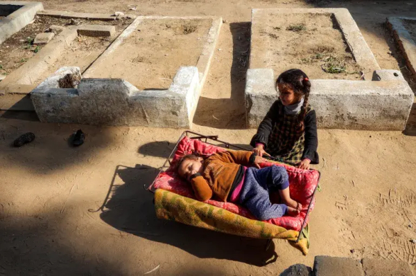 A girl rocks a makeshift metal cradle where a child is lying, as families displaced by conflict take shelter by graves in a cemetery in Deir el-Balah in the central Gaza Strip on January 12, 2025 [Eyad Baba/AFP]