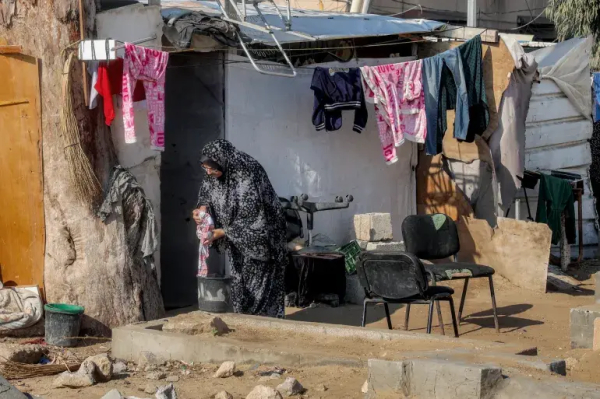 A woman washes clothes by hand on a grave at a cemetery where families displaced by conflict are taking shelter, in Deir el-Balah in the central Gaza Strip on January 12, 2025 [Eyad Baba/AFP]