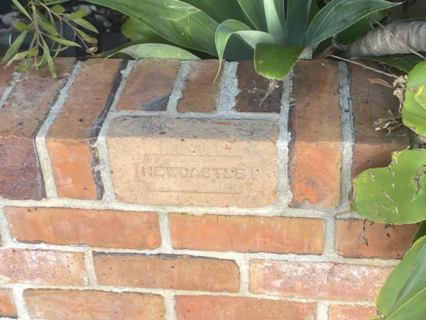 Low brick garden retaining wall with an old brick inset on the top row. The brick is stamped with NEWCASTLE. It was outside one of the older terrace houses.