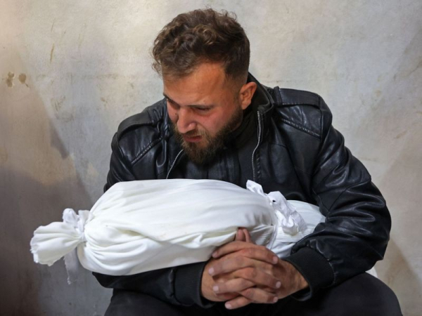 Foto van een Gazaanse man met een, door de Israeli Destruction Forces, in concentratiekamp Gaza, geliquideerd Gazaans kind in een witte zak in zijn armen.