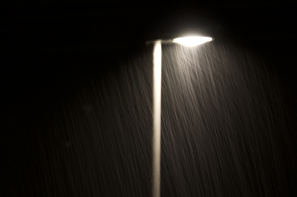 Eine Straßenlaterne bei Nacht. Der Regen ist in Form von Strichen im Lichtkegel der Laterne zu erkennen.