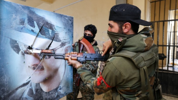 A fighter affiliated with Syria’s new administration bayonets a portrait of toppled president Bashar al-Assad at the defunct Mezzeh military prison in Damascus