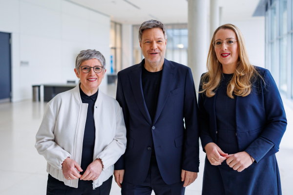 Man sieht ein Foto von Britta Haßelmann, Robert Habeck und Katharina Dröge, die nebeneinander stehen und in die Kamera lachen.