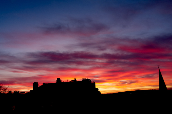 A landscape-oriented colour photograph of the sky over Edinburgh tonight.

At the bottom of the picture is the silhouette of the skyline from my flat looking south-west, with a church steeple at the far right and the tenement opposite most of the bottom left.

Above that, the sky is coloured, ranging from orange near the bottom (to the right of the tenement), through deep red and mauve clouds; other cloudss are dark grey. Where there are no clouds the sky is various shades of blue, from palid blue low down to dark intense blue near the top.