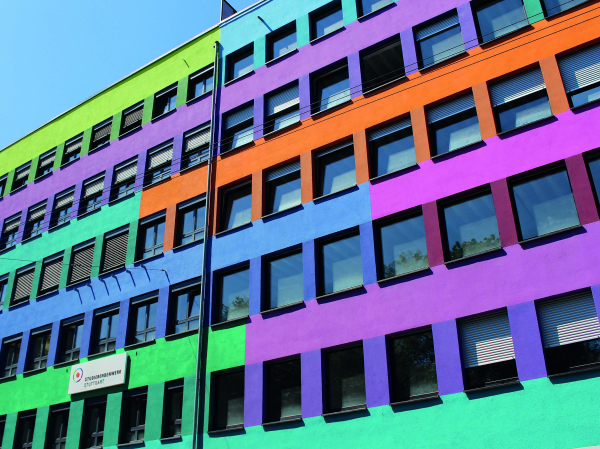 Das Gebäude unserer Verwaltung. Die Fassade ist bunt gestrichen: Grün, Petrol, Lilia, Orange und Blau. Ein Schild mit der Aufschrift "Studierendenwerk Stuttgart" ist angebracht.