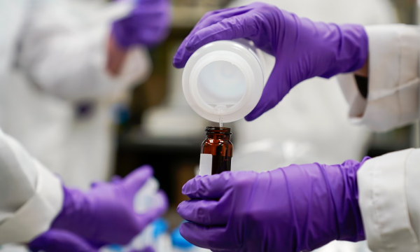 Photo: someone pouts liquid from a plastic container into a glass bottle. Caption: A researcher pours a water sample for experimentation during drinking water and PFAS research. Photograph: Joshua A Bickel/AP