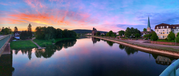 Aussicht von der Holzmindener Weserbrücke in Richtung Kiekenstein, der Fluß unter einem dramatischen Sonnenuntergangshimmel im rechten Bild prägnante Gebäude der Stadt-Ansicht, u.a. der Turm der Kirche, die Silhoutte des Kornspeichers (ehem. Reichsnährstandsspeicher) und der Weserkai.