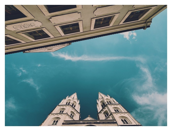 An upwards perspective showing a cathedral and a house with windows. Blue sky in the middle.