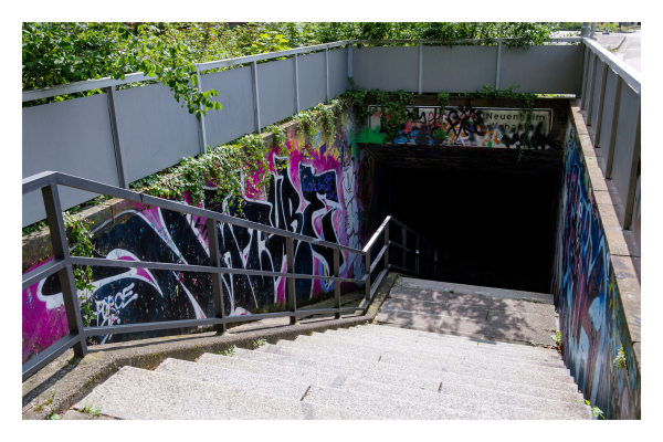 Foto im Querformat. Treppen gehen hinab zu einer U-Bahn Haltestelle bzw zu einem Tunnel. Überall ist Graffiti an den Wänden. Wo die Treppen enden beginnt schwarz. Es ist nicht zu erkennen, was im Tunnel ist. 