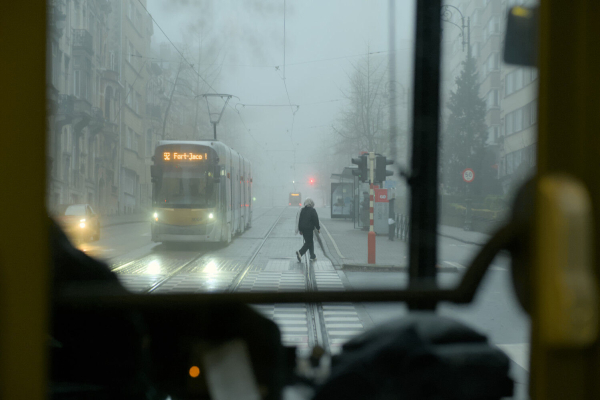 Photo of a person crossing the tram tracks on a foggy, grey day, taken from inside a tram through its front window.