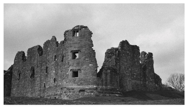 Grainy and dark black and white photograph of crumbling old castle walls.