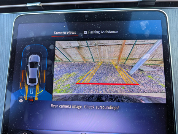 Photo of the central infotainment screen inside a Mercedes EQE, showing the reversing camera view and parking sensor status display.