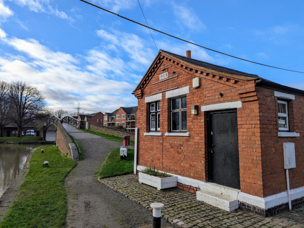 Photo of a small red brick building at the end of a footbridge.