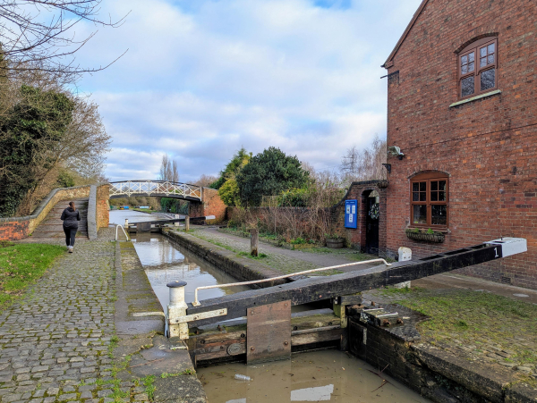 Photo of a small hand operated canal lock, with a bridge over the canal beyond it.