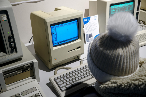 Photo of an original 1980's Apple Macintosh computer with a child sitting at it, drawing a picture in a paint program.