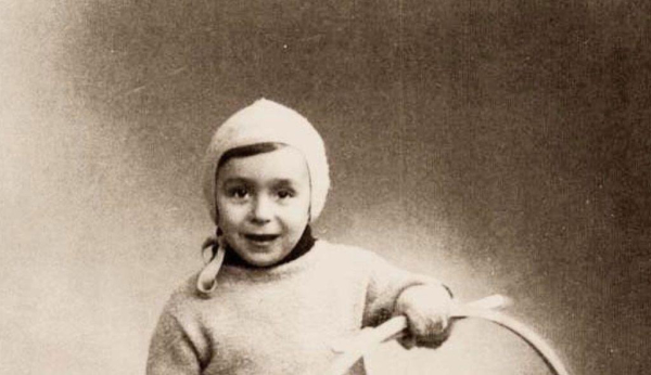 Black and white historical photo of a young child wearing a knit cap and sweater, smiling and holding a hoop.