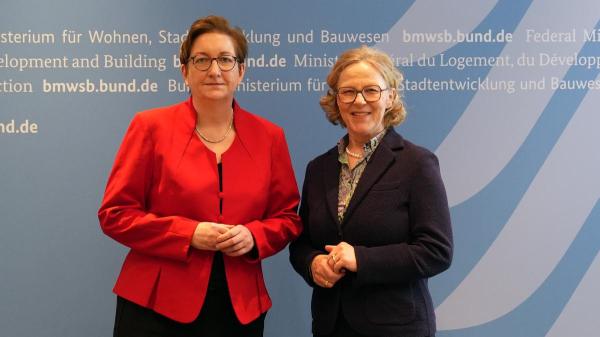 Bundesbauministerin Klara Geywitz neben der sächsischen Staatsministerin für Infrastruktur und Landesentwicklung, Regina Kraushaar. Beide stehen vor einer blauen Wand und schauen in die Kamera.