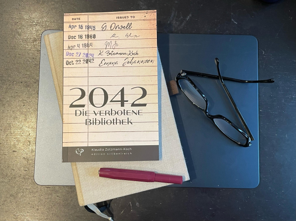 Foto der gedruckten Novelle „2043 - Die verbotene Bibliothek“, die neben Lesebrille und Kaweco-Füller auf meinem Notizbuch und dem Laptop liegt 