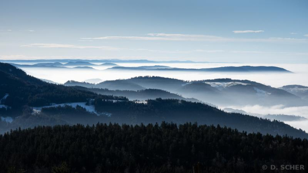 About ten successive layers of wooded hilltops separated by seas of shiny white clouds trapped in the valleys under a blue sky.