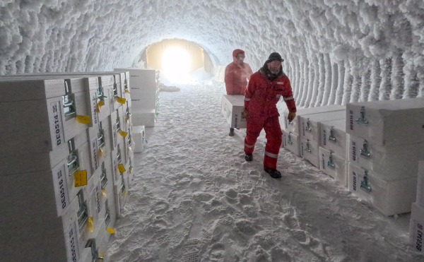 Zwei Männer in roten Overalls tragen eine Kiste im Eiskernlager.