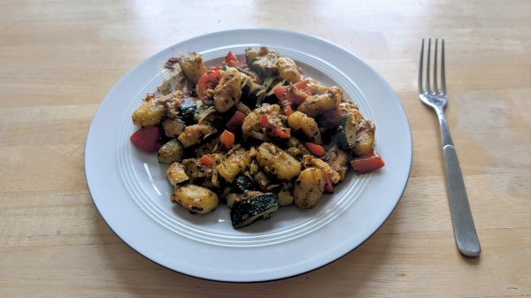 Ein Teller mit veganen Gnocchi mit Zucchini, Paprika und Lauch. Mit einer Spinat & Pinienkerne Soße und Ingwer und einem Spritzer Zitrone plus Tomatenmark.