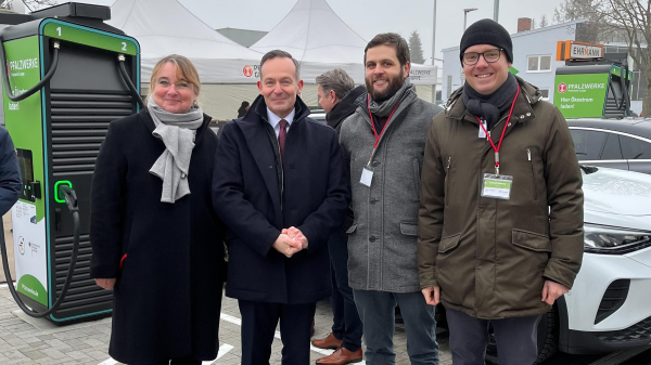 © NOW GmbH. Auf dem Gruppenbild steht ganz links Dagmar Fehler. Volker Wissing steht in der Mitte, rechts neben dem Minister haben sich Felix Steck und Conrad Hammer von der Nationalen Leitstelle Ladeinfrastruktur der NOW GmbH positioniert. Im Hintergrund ist eine Ladesäule erkennbar.