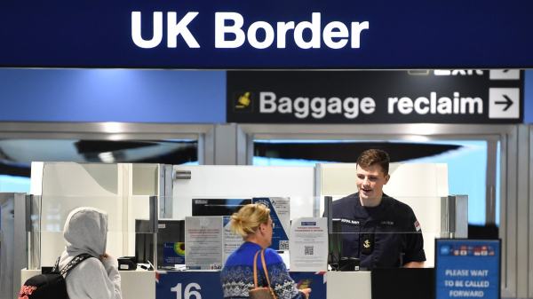 Photo: two people que in front of a check on visas at an airport