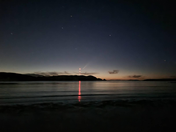 Calm bay, reflecting red pilon lights, sun just gone down on a clear warm summer's evening, and the comet can be seen wooshing away.