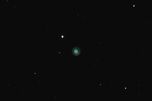 Planetary nebula NGC 2392 shown as a greenish disk in front of a sparse star field. Some colorful details are visible in the disk.