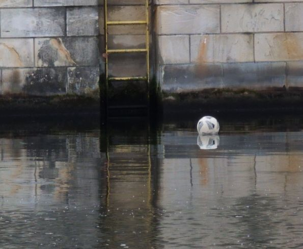 auf einem Fluss schwimmt ein weißer Ball mit grauen Mustern, im Hintergrund ist eine Wand aus rechteckigen Steinen zu sehen, an welcher eine gelbe Leiter angebracht ist. Der Ball ist nun an der Leiter vorbei, leider ;-)