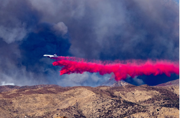 Low brown hills in LA, no structures, blue sky with white smoke, thin in places.  Low over the hills a DC10 dropping magenta colored retarded. Photo David Crane LA Times