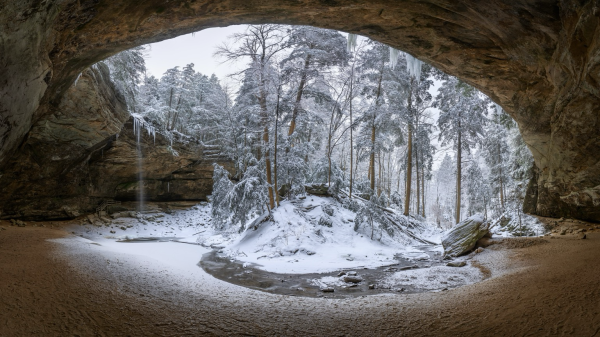 This is an image of Ash Cave in the Hocking Hills State Park in southwest Ohio. This winter scene shows a small stream meandering under the cave and through the snow covered trees. 