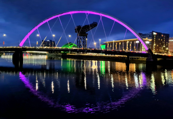 An arch-shaped bridge lit up at nightfall and reflected in the still waters below.